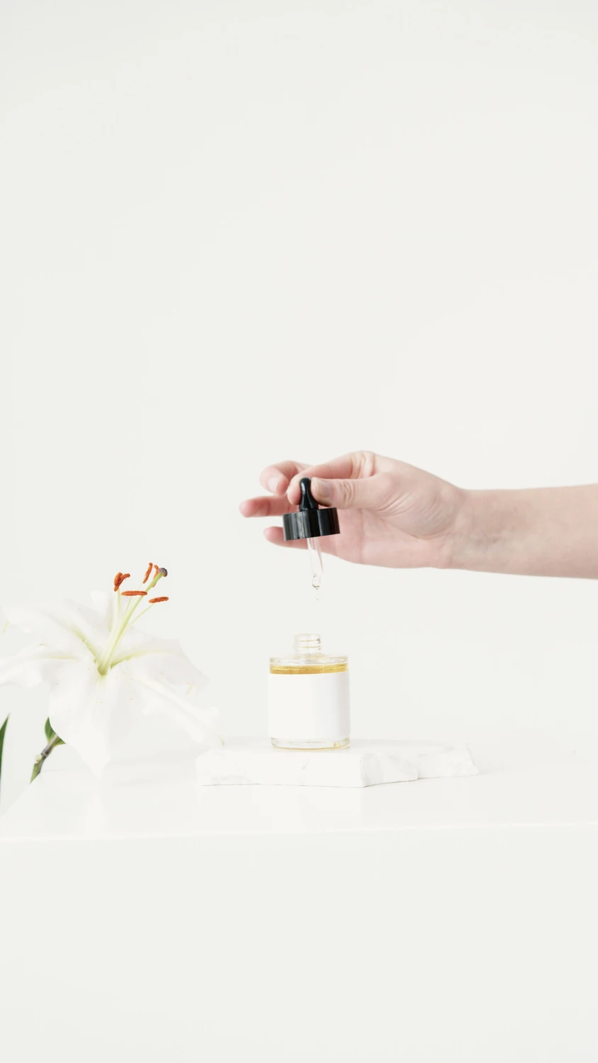 Linden-Apotheke - Pharmazeutische Dienstleistungen & Online-Bestellung - Frauenhände halten eine Pipette mit Kosmetikserum vor hellbraunem Hintergrund im Sonnenlicht. Nahaufnahme, Platz für Text. Konzept der Körperpflege.
